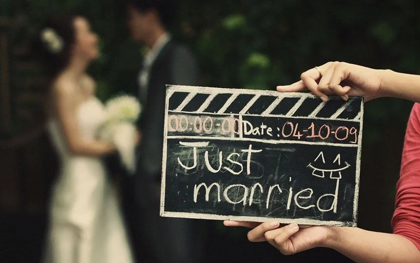 Para młoda w tle, na pierwszym planie klaps filmowy z napisem Just married