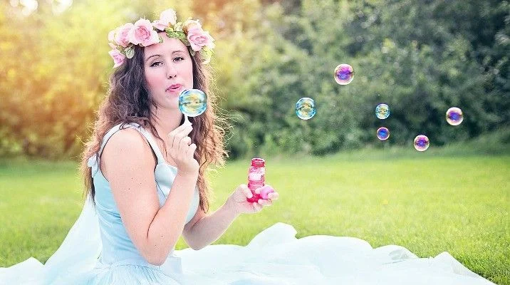 Dziewczyna w wianku z kwiatów puszczająca bańki mydlane na trawie