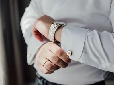 Pan Młody z obrączką i zegarkiem na ręce zapina spinkę przy mankiecie białej koszuli
