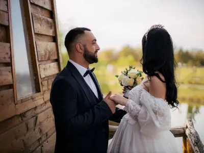 Pan Młody trzyma Pannę Młodą za rękę przy drewnianym domku nad stawem