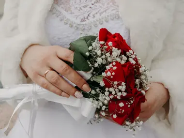 Panna młoda w białym futerku trzyma bukiet z czerwonych róż i gipsówki
