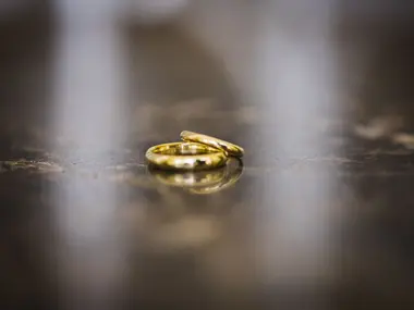 Dwie złote obrączki ślubne leżące na ciemnej, lśniącej powierzchni z rozmytym tłem