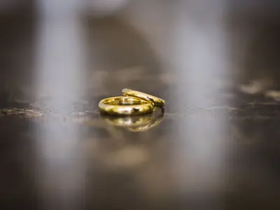 Dwie złote obrączki ślubne leżące na ciemnej, lśniącej powierzchni z rozmytym tłem