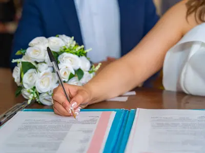 Panna młoda podpisuje dokumenty w urzędzie, obok leży bukiet białych róż
