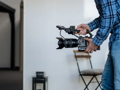Operator trzyma profesjonalną kamerę filmową w jasnym wnętrzu z krzesłem i lampionem