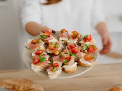 Kobieta podaje talerz koreczków z szynką parmeńską, serem i pomidorkami koktajlowymi