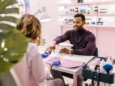 Mężczyzna w bordowym golfie podczas zabiegu manicure w jasnym salonie kosmetycznym