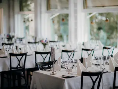 Jasna sala restauracji z nakrytymi białymi obrusami stołami przygotowanymi na przyjęcie