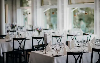 Jasna sala restauracji z nakrytymi białymi obrusami stołami przygotowanymi na przyjęcie