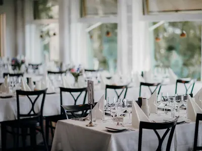 Jasna sala restauracji z nakrytymi białymi obrusami stołami przygotowanymi na przyjęcie
