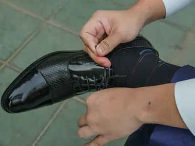 Pan Młody w koszuli wiąże lakierowane buty, spod nogawki widać ciemną skarpetkę w kolorowe paski