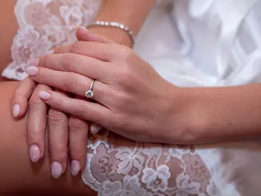 Zadbane dłonie Panny Młodej z pierścionkiem zaręczynowym i jasnym manicure na koronkowej sukni