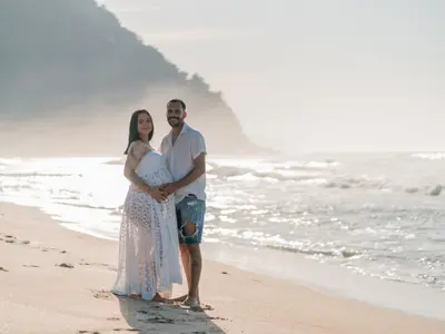 Kobieta w ciąży w koronkowej sukience obejmowana przez partnera na plaży nad morzem