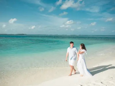 Młoda para w bieli spaceruje boso po plaży nad turkusowym morzem