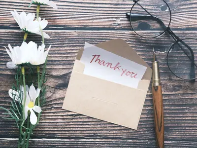 Koperta z kartką „Thank you” i białe kwiaty na drewnianym stole