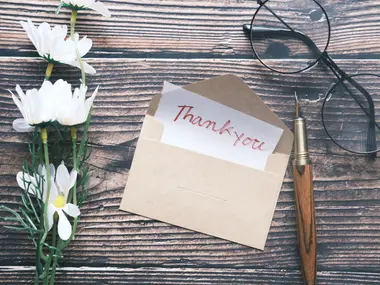 Koperta z kartką „Thank you” i białe kwiaty na drewnianym stole