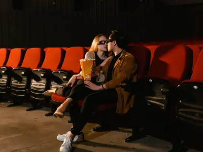 Para w okularach 3D z popcornem siedzi przytulona w pustej sali kinowej
