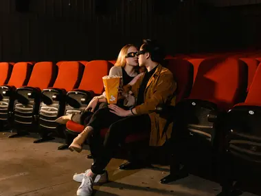 Para w okularach 3D z popcornem siedzi przytulona w pustej sali kinowej