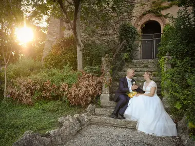 Para młoda siedzi na kamiennych schodach w zarośniętym ogrodzie przy zachodzącym słońcu