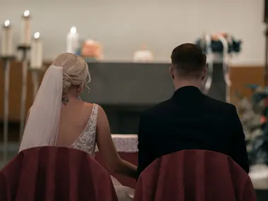 Para młoda siedzi tyłem przy ołtarzu kościoła, panna młoda w długim welonie