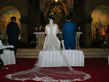 Panna młoda w długim welonie i pan młody stoją przed ołtarzem na czerwonym dywanie