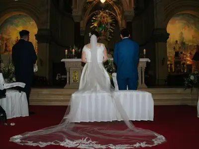 Panna młoda w długim welonie i pan młody stoją przed ołtarzem na czerwonym dywanie