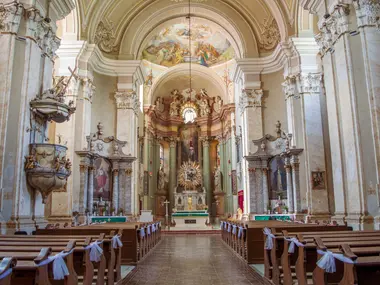 Barokowe wnętrze kościoła z ławkami przystrojonymi białymi kokardami, w głębi złocony ołtarz