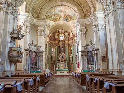 Barokowe wnętrze kościoła z ławkami przystrojonymi białymi kokardami, w głębi złocony ołtarz