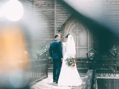 Para młoda przed drewnianą kaplicą z gotyckimi drzwiami, panna młoda trzyma bukiet