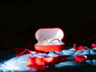 Dwie złote obrączki w czerwonym pudełku wśród rozsypanych płatków czerwonych róż