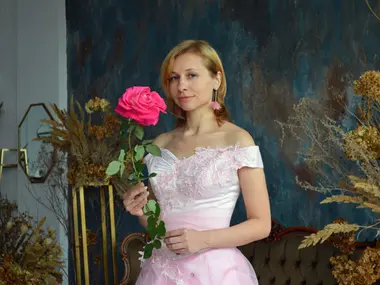 Kobieta w różowej sukni ślubnej z różą w dłoni, w tle suszone kwiaty