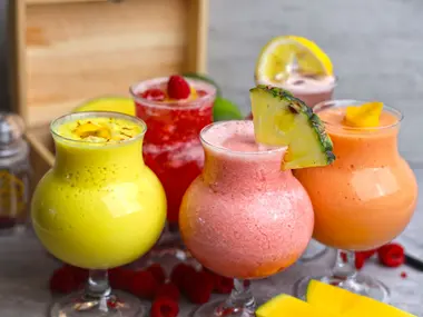 Kolorowe bezalkoholowe koktajle owocowe udekorowane ananasem, cytryną i malinami, obok plastry mango