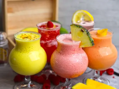 Kolorowe bezalkoholowe koktajle owocowe udekorowane ananasem, cytryną i malinami, obok plastry mango