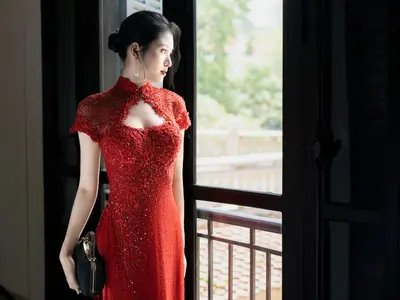 Kobieta w czerwonej koronkowej sukni w stylu qipao stoi przy oknie balkonowym