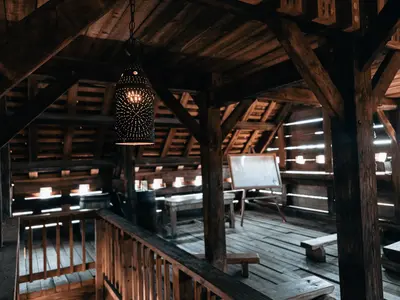 Drewniane wnętrze pod belkowanym dachem z ławami, balustradą i wiszącą ażurową latarnią