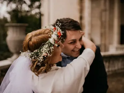 Panna Młoda w wianku z gipsówki i drobnych czerwonych kwiatów obejmuje roześmianego Pana Młodego