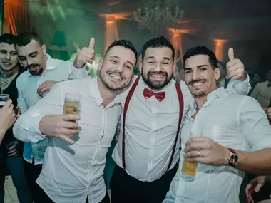 Mężczyzna w czerwonej muszce i szelkach bawi się z kolegami, którzy unoszą kciuki