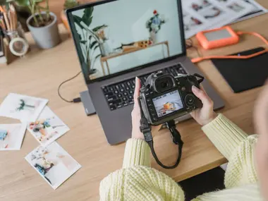 Fotograf przegląda zdjęcia na ekranie aparatu przy laptopie i rozłożonych odbitkach