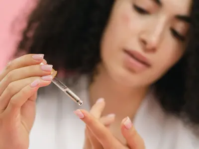 Kobieta nakłada pipetą odżywkę na zadbane paznokcie pomalowane na jasnoróżowy kolor