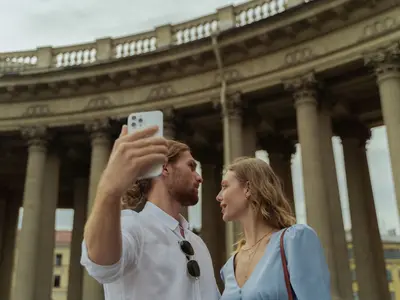 Para robi sobie selfie smartfonem przed półkolistą kolumnadą zabytkowej budowli
