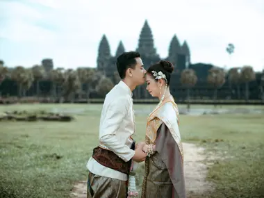 Pan młody całuje w czoło pannę młodą w tradycyjnych strojach khmerskich przed Angkor Wat