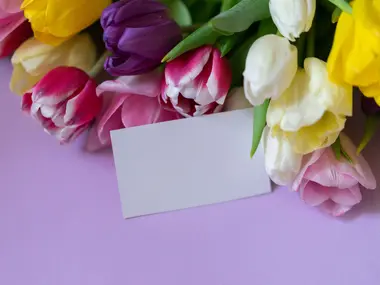 Bukiet kolorowych tulipanów i pusta kartka na życzenia na liliowym tle