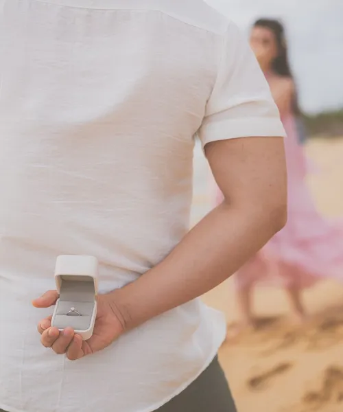 Mężczyzna na plaży chowa za plecami pierścionek przed oświadczynami