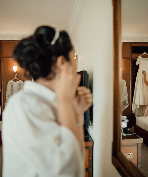 Panna młoda poprawia suknię przed lustrem w pokoju hotelowym
